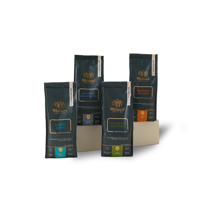 Four upright coffee bags from Whittard, each showcasing a different blend—Santos & Java, Guatemala Elephant, Whittard House Blend, and Monsoon Malabar—are arranged on a beige stand. Perfect for those who enjoy robust flavors, The Big, Bold Coffee Subscription invites you to explore Whittard’s rich collection or discover new favorites delivered straight to your door.