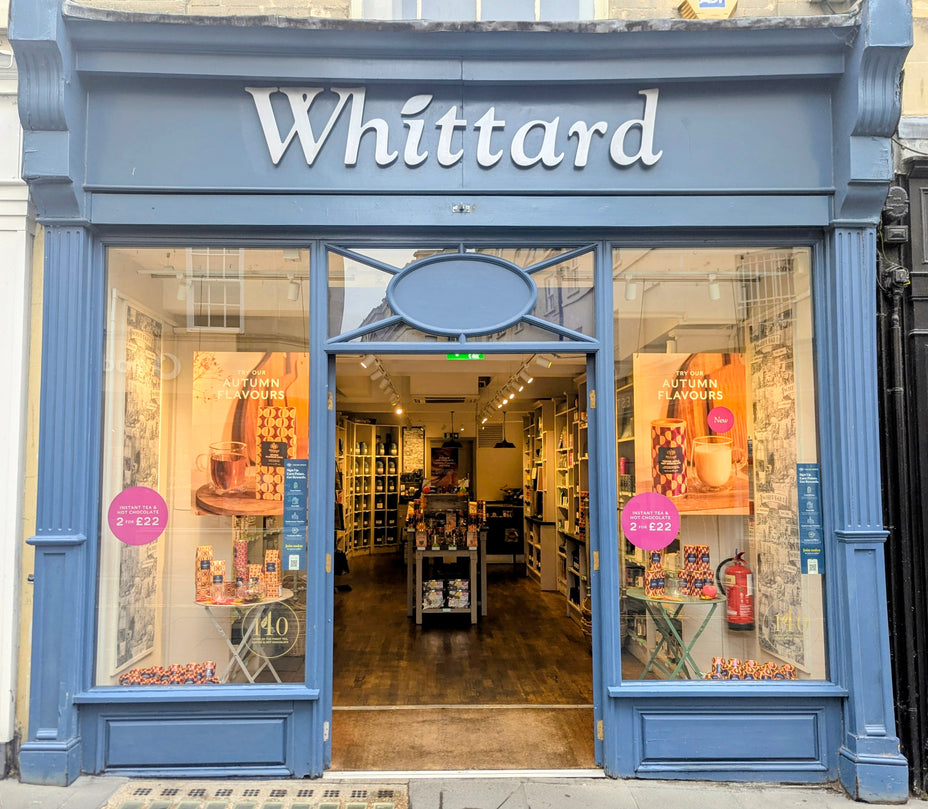 Storefront of Whittard, a tea and coffee shop with large windows displaying autumn flavors promotions and products inside on wooden shelves, with a blue-painted exterior.