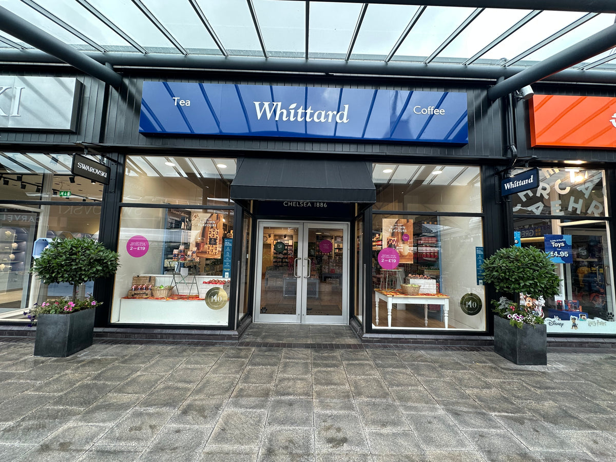 A Whittard tea and coffee shop with glass doors, large blue signage, and potted plants outside. The shop interior displays shelves of products and promotional signs in the windows.
