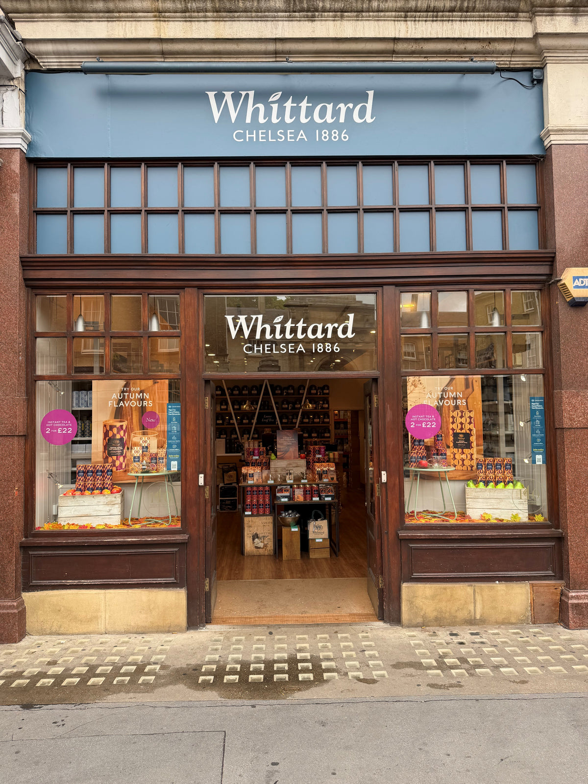 Storefront of Whittard Chelsea 1886, featuring large windows displaying tea and gift products, with an open door inviting shoppers inside. The stores name is prominently displayed above the entrance.