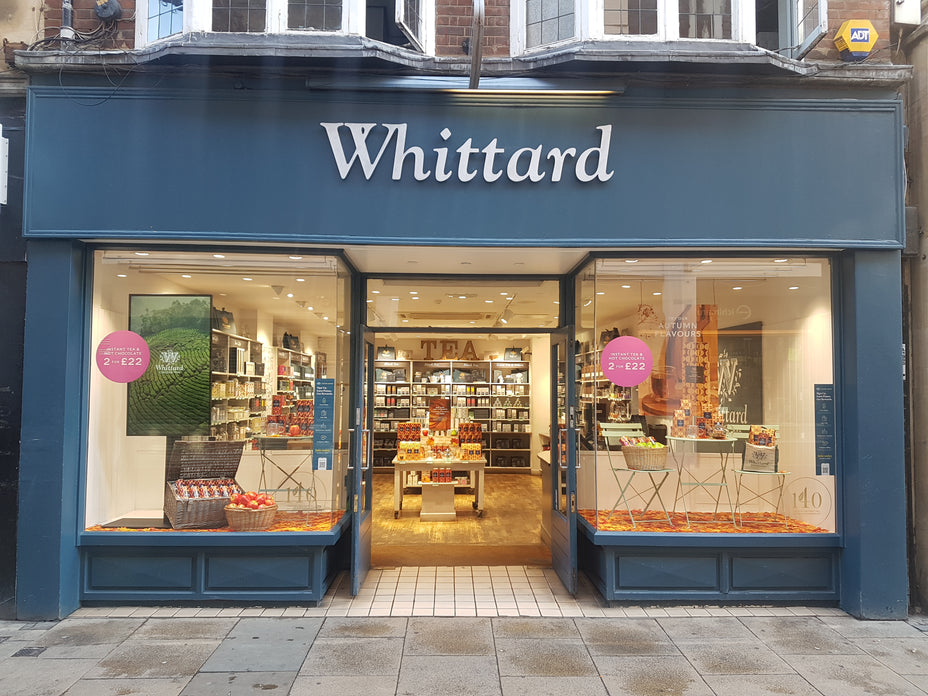 Front view of the Whittard store, displaying tea products in the windows and inside. The store is well-lit, with shelves full of goods and promotional signs on the glass.