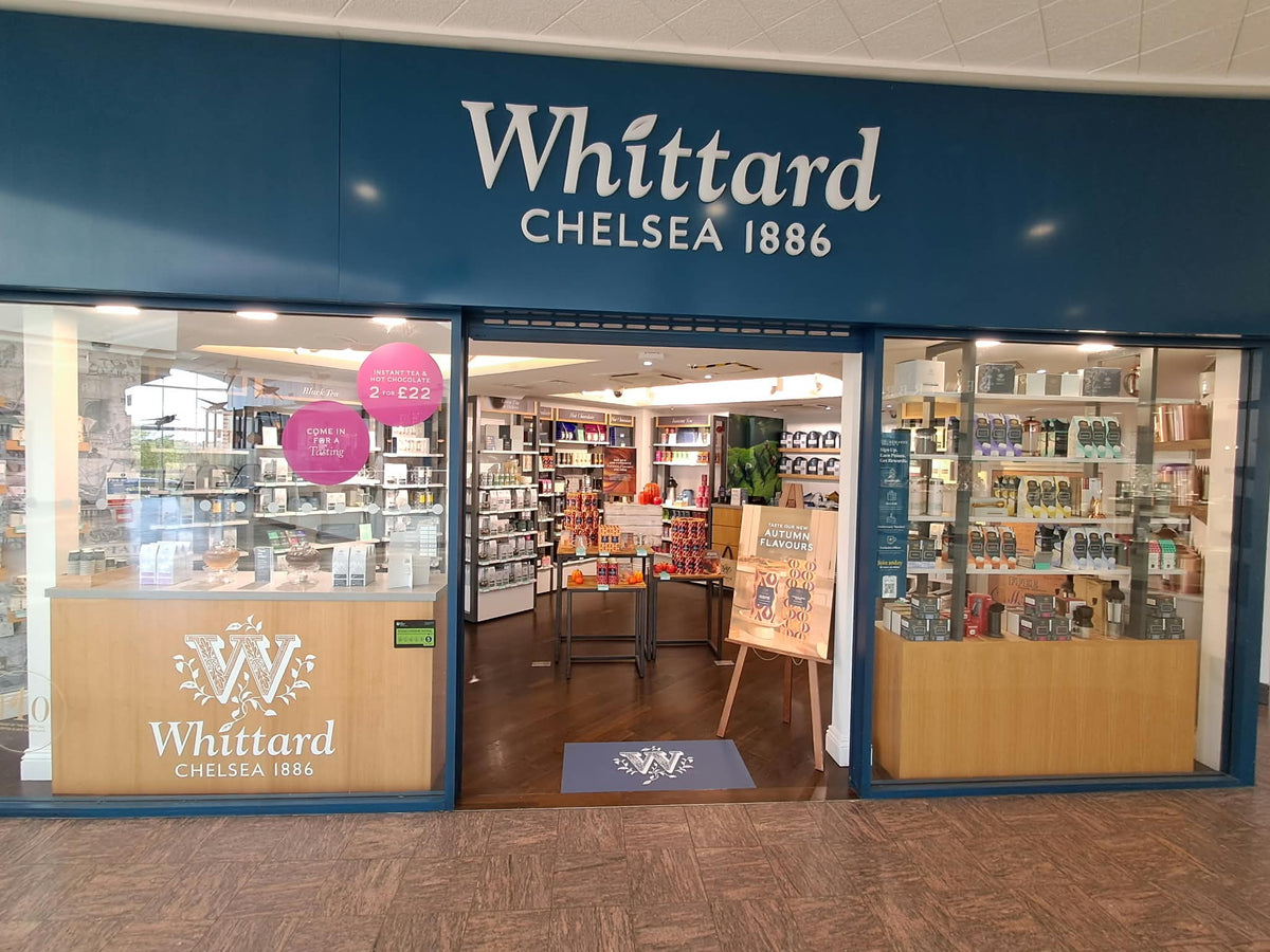The exterior of a Whittard of Chelsea store, featuring large glass windows displaying tea and coffee products, with a clear sign reading Whittard CHELSEA 1886 above the entrance.