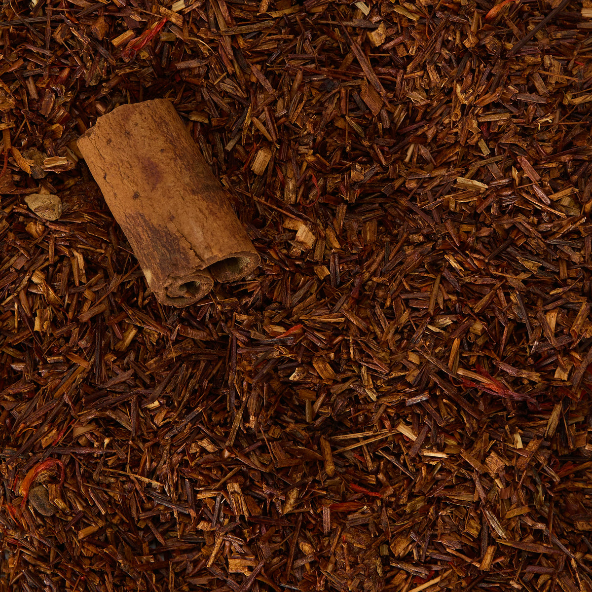 A cinnamon stick resting on a bed of Fireside Rooibos Loose Infusion loose-leaf herbal tea.