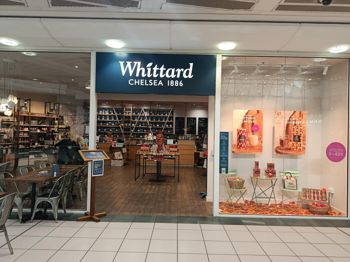 Shopfront of Whittard of Chelsea, established 1886, with a window display featuring tea products. Indoor seating and shelves filled with various packaged goods are visible inside the brightly lit store.