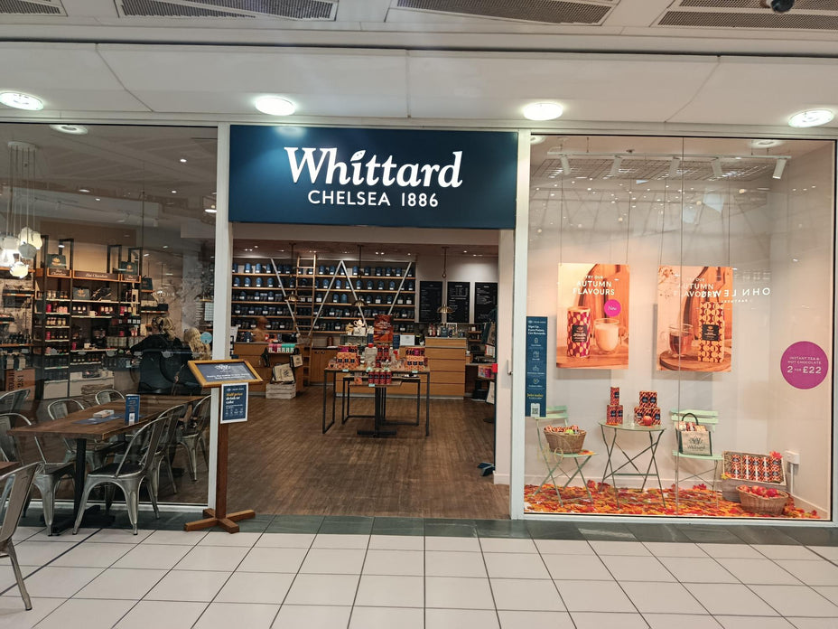 Shopfront of Whittard of Chelsea, established 1886, with a window display featuring tea products. Indoor seating and shelves filled with various packaged goods are visible inside the brightly lit store.