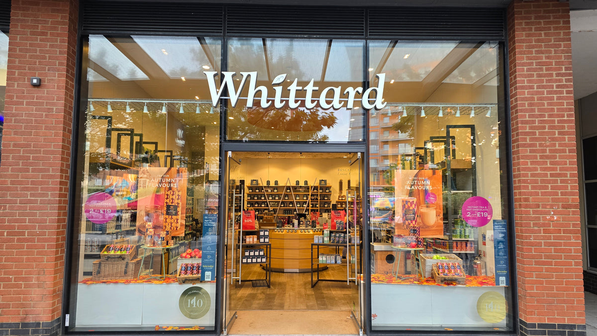 Storefront of Whittard, a tea and coffee shop, with glass windows displaying products and autumn-themed decorations. The shop interior with shelves and displays is visible through the open entrance.