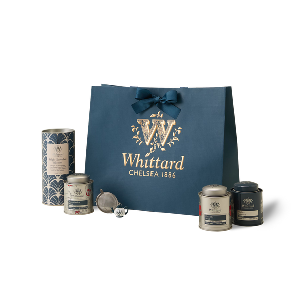 The Best of British Gift Box features a blue Whittard Chelsea 1886 gift bag, three tea tins, a tea infuser, and a tall tea canister elegantly arranged on a white background—an ideal British tea gift set for lovers of premium loose leaf teas.