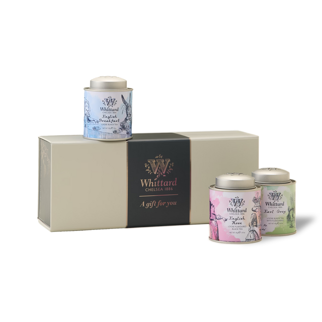 The Alice In Wonderland Mini Caddy Gift Box is a whimsical tea gift set featuring three pastel tea tins—blue, pink, and green—adorned with charming Alice in Wonderland designs. Nestled beside a cream-colored gift box with a black band labeled “A gift for you,” each tin holds premium loose leaf black teas, perfect for an enchanting teatime experience.