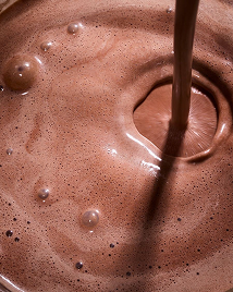 Chocolate milk being poured, creating bubbles and ripples on the frothy surface.