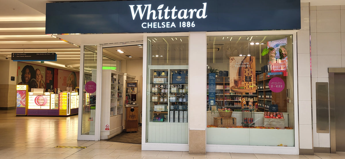 Whittard Chelsea 1886 storefront in a shopping mall, displaying tea and merchandise in the window with sale signs and shelves visible inside.