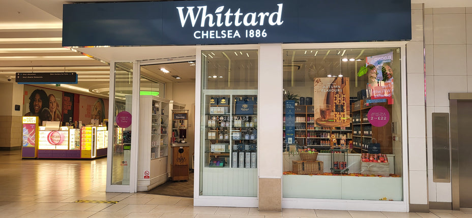 Whittard Chelsea 1886 storefront in a shopping mall, displaying tea and merchandise in the window with sale signs and shelves visible inside.