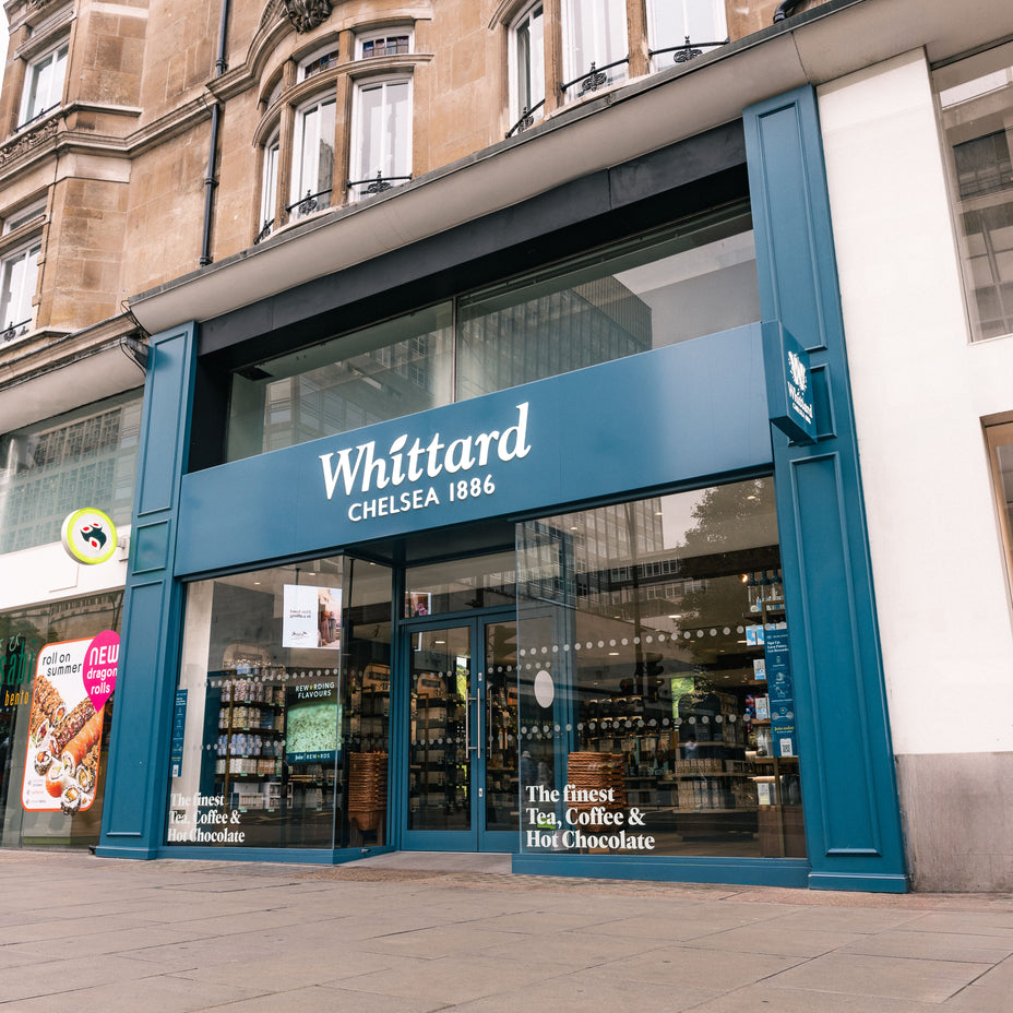 The exterior of a Whittard of Chelsea store, with large glass windows and a blue sign. Displays inside show tea, coffee, and hot chocolate products.