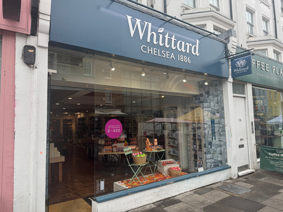 Whittard Chelsea 1886 shopfront with large glass window displaying tea and gift items. Sign above the entrance. Street view with neighboring businesses visible.