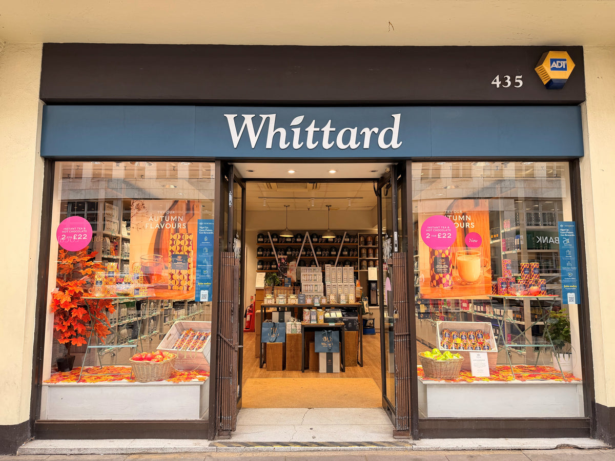Whittard storefront with large window displays, autumn-themed decorations, and shelves of teas and gifts visible inside. Promotional signs are in the windows.