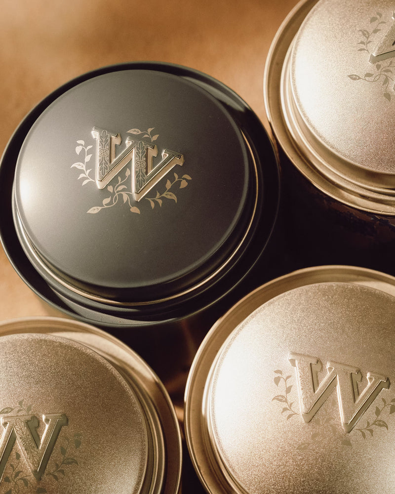 Three circular tea tins with metallic lids, each embossed with a decorative letter W and floral accents.