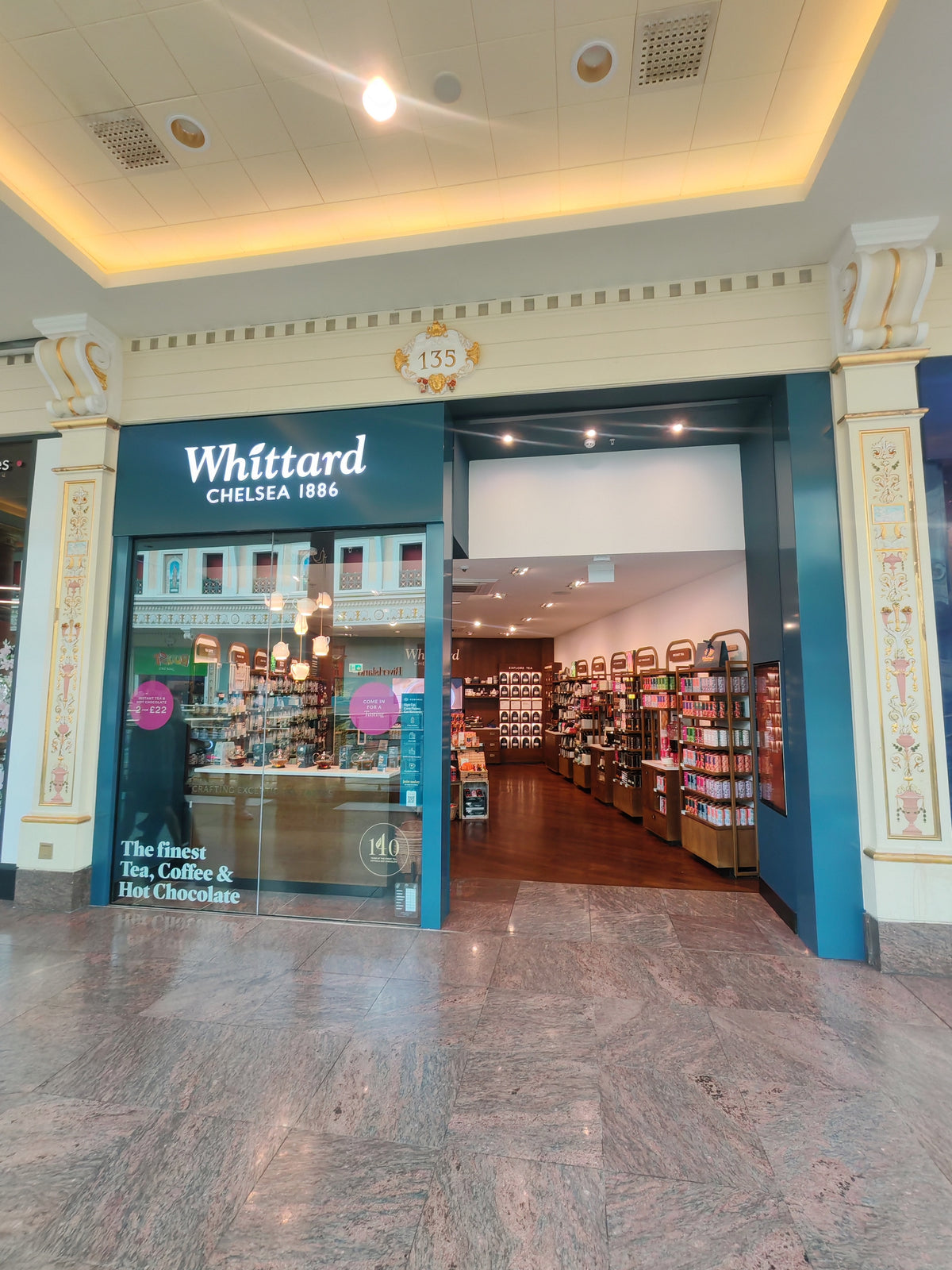 The image shows the entrance to a Whittard Chelsea 1886 store in a mall, with tea, coffee, and hot chocolate products displayed inside and signage above the glass door.