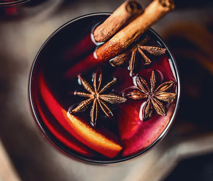 A close-up of a glass of mulled wine with orange slices, star anise, and cinnamon sticks floating on top.